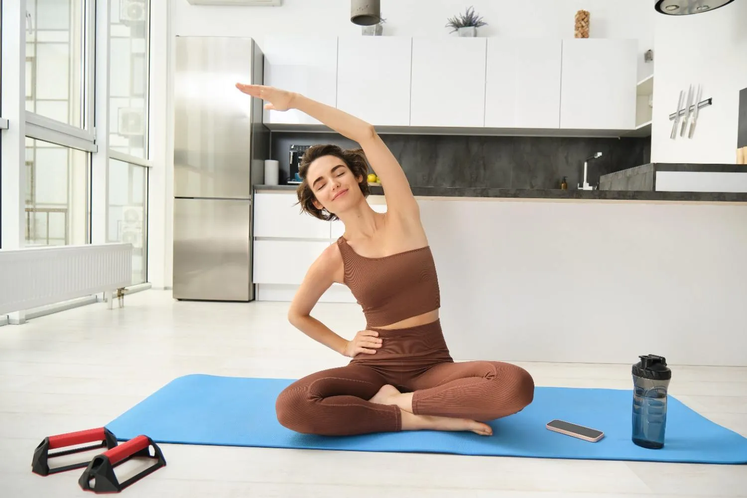 A woman stretching on a mat in her kitchen before breakfast