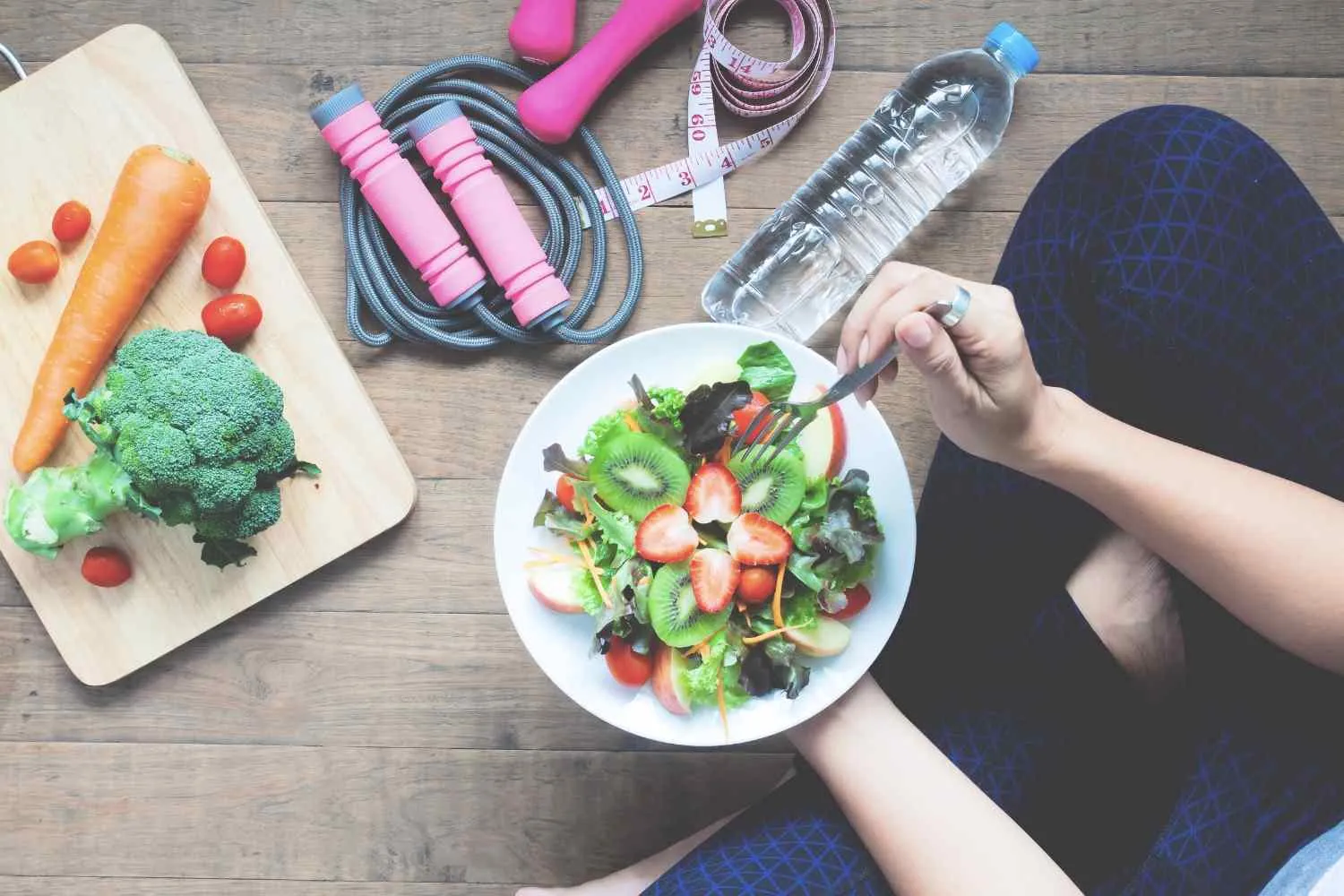A bowl of salad beside a water bottle, skipping rope and fresh vegetables